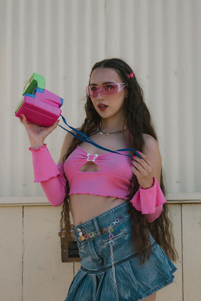 Mastering the First Impression: Your intriguing post title goes here Fashionable young woman in retro outfit holding a colorful vintage camera outdoors. Y2K style.
