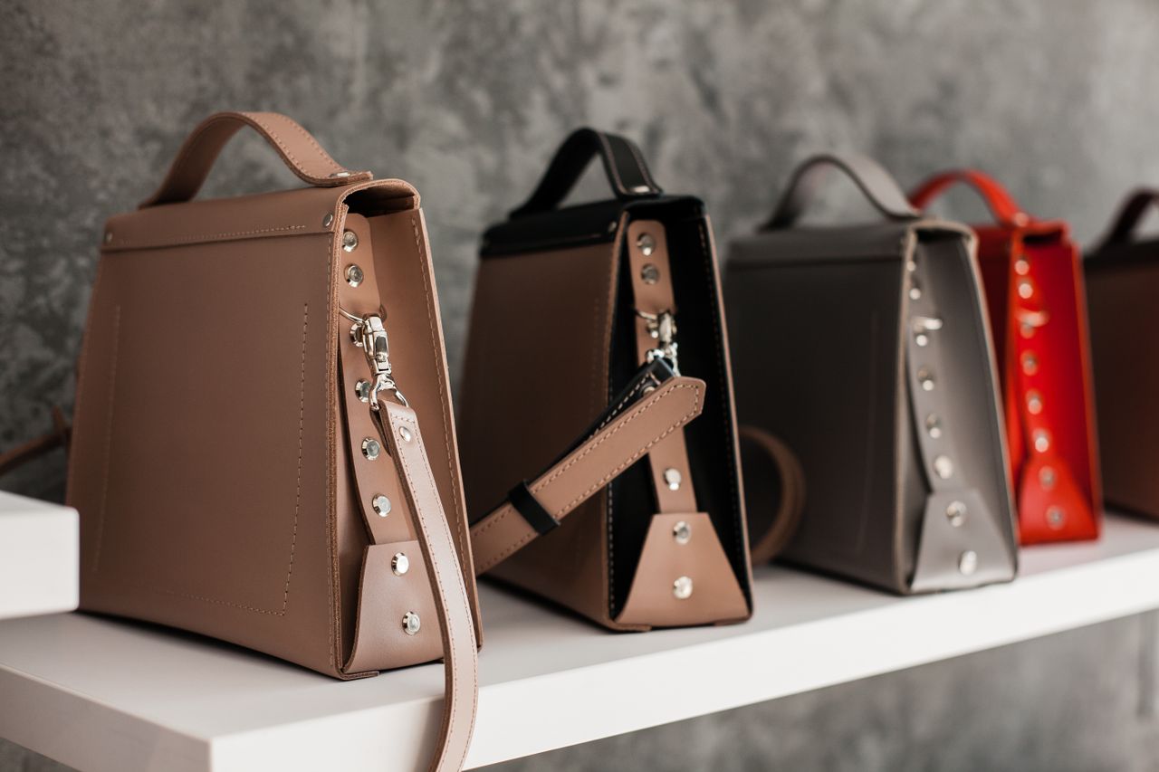 team-04 Luxury leather handbags displayed on a white shelf, showcasing minimalistic design and various colors.